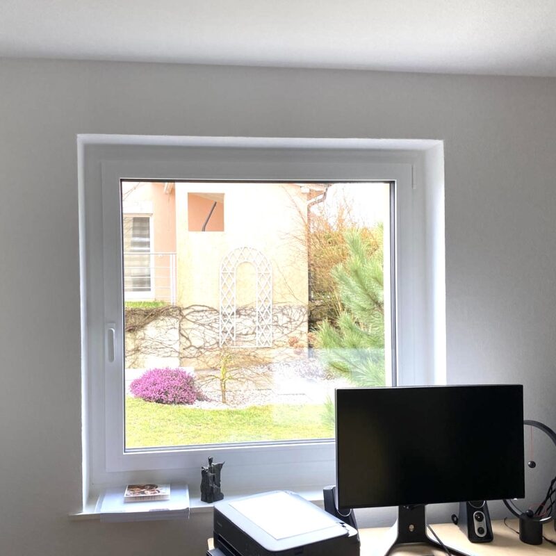 Vue jardin depuis fenêtre avec bureau et écran
